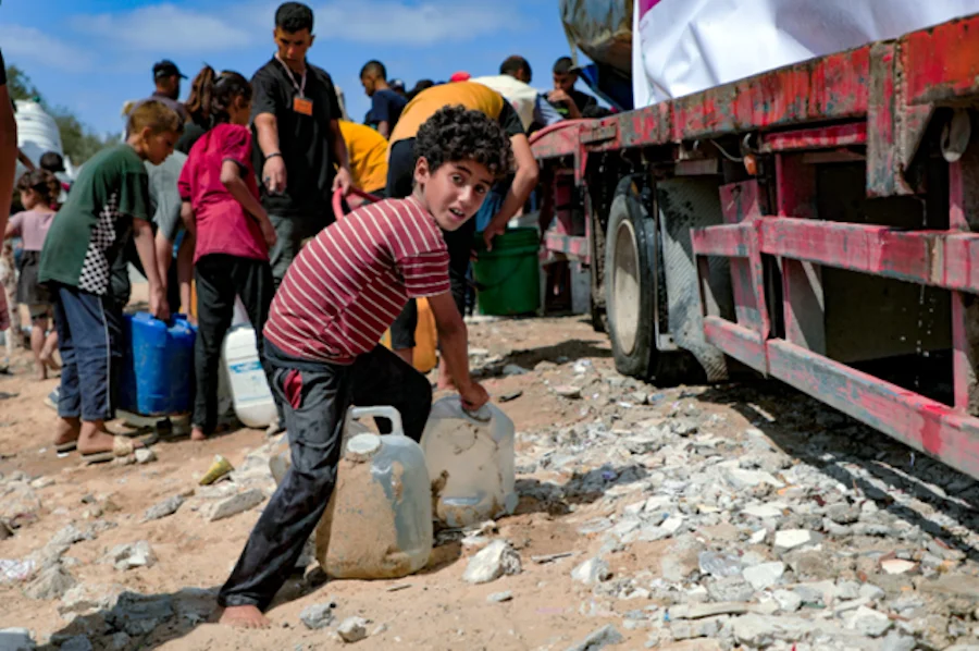 Un niño recoge garrafas de agua potable durante el alto el fuego en Gaza | Foto de Plan International / Taawon