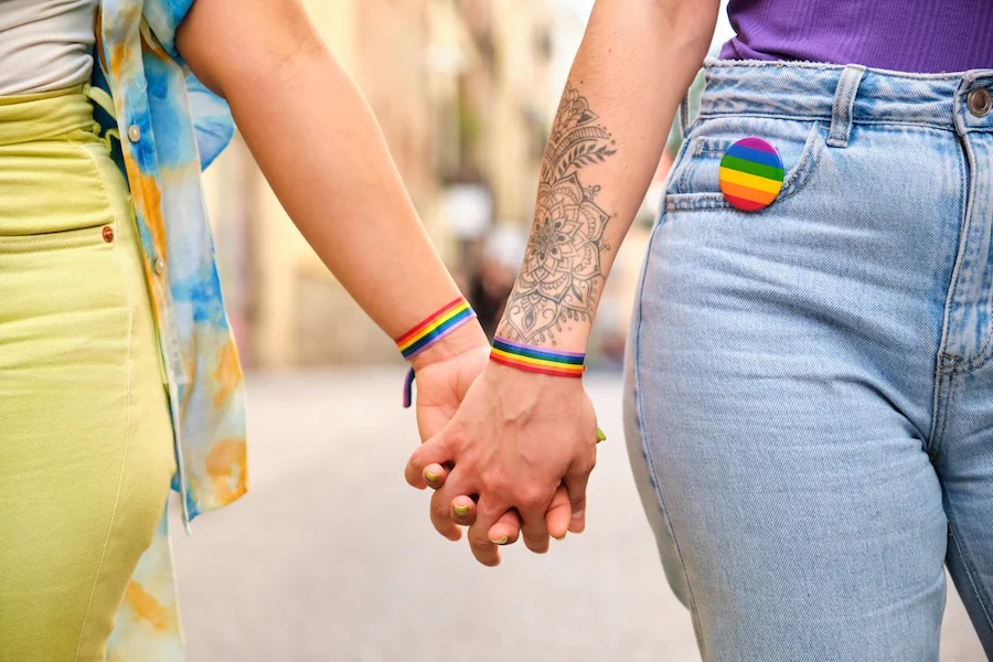 Detalle de dos personas de la mano con la bandera Lgtbi+ | Foto de 123RF/cladanifer